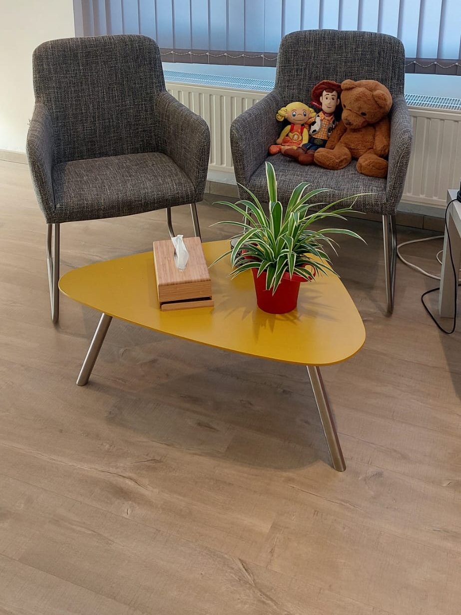 Zithoek in de praktijk met twee fauteuils, een gele salontafel en knuffels